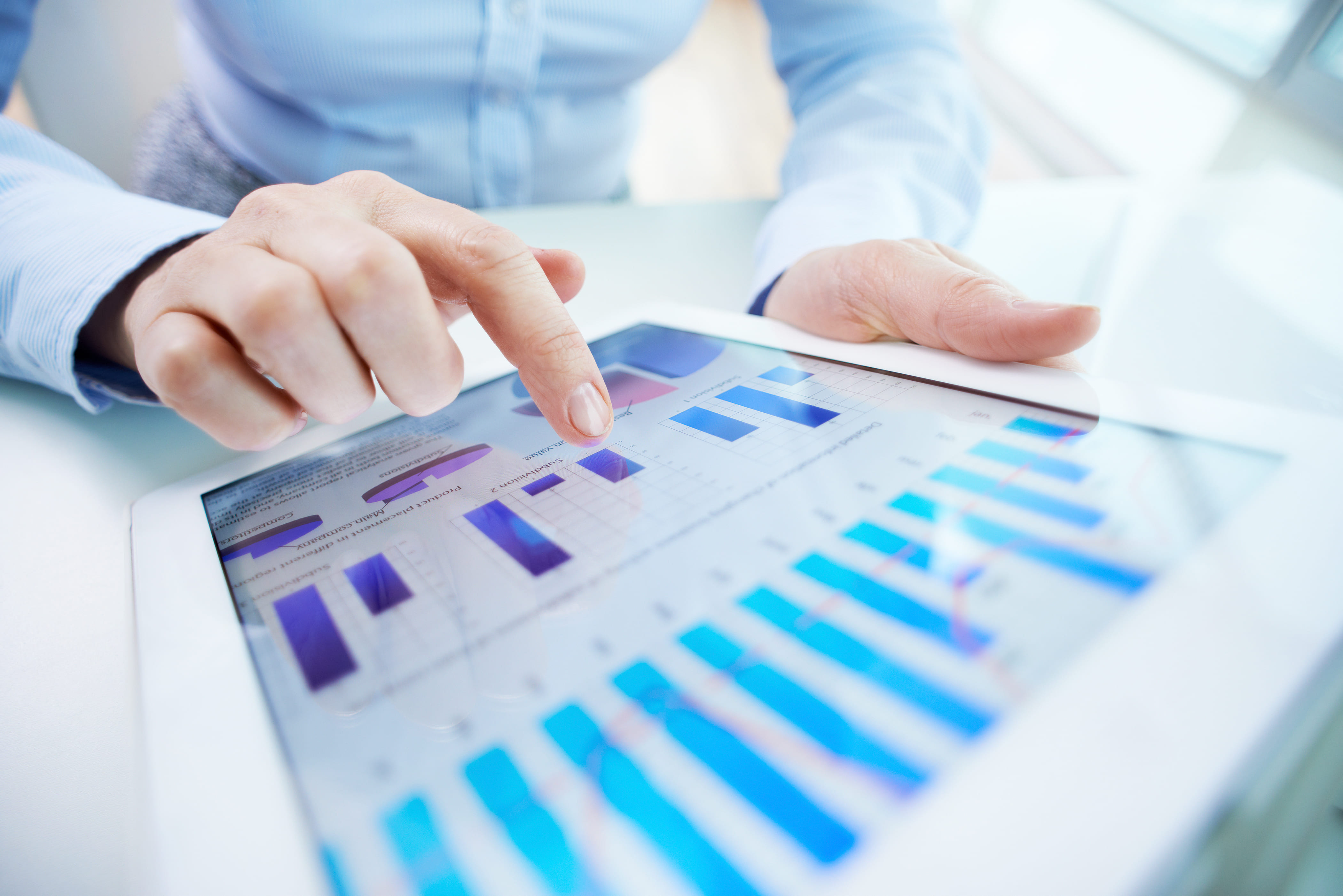Mão segurando um tablet com gráficos financeiros.