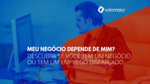 Homem diante do computador e, ao seu lado, uma pilha de pastas e papéis.