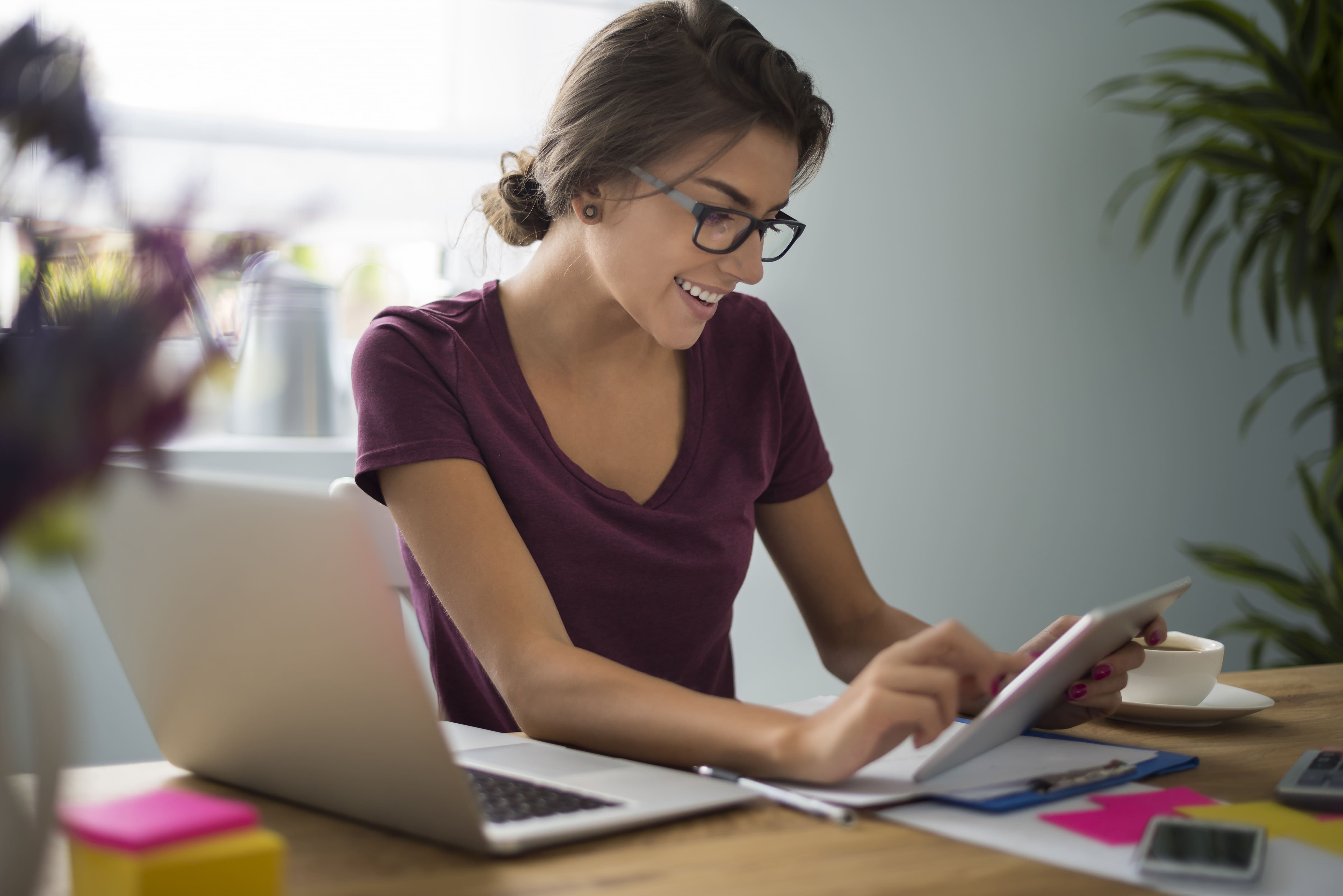 Mulher empreendedora com laptop, tablet e papeis sobre a mesa de trabalho.